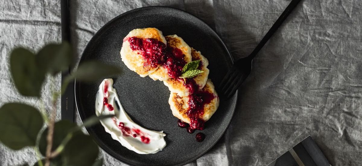 Tasty pancakes topped with fresh berry sauce on a ceramic plate, perfect for a gourmet breakfast.